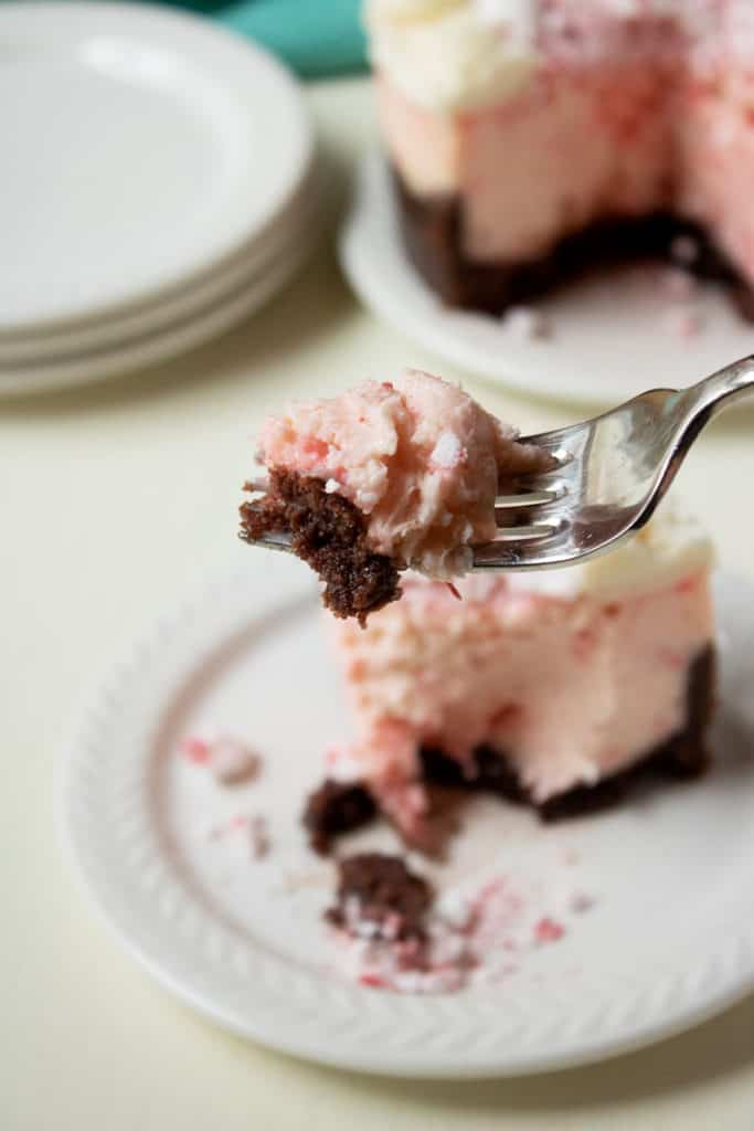 fork with a bite of peppermint cheesecake on it and peppermint cheesecake on a plate in the background