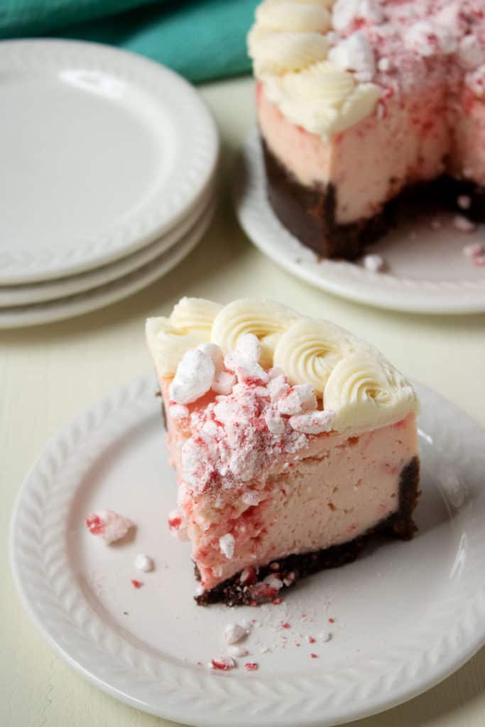 slice of peppermint cheesecake on a white plate with whole cheesecake in the background