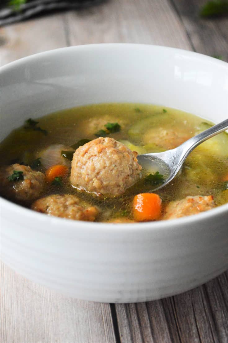 meatball soup in white bowl with spoon picking up a meatball