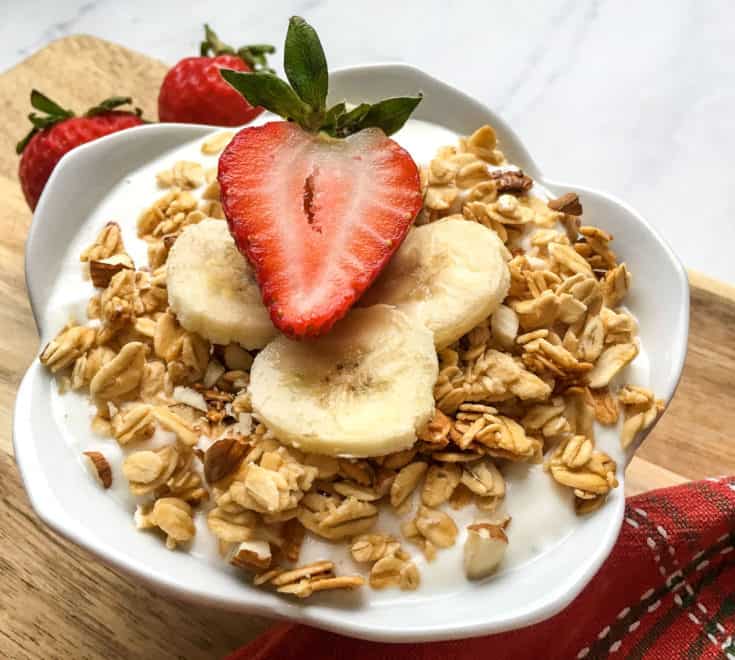 yogurt with granola, bananas and strawberries in white bowl