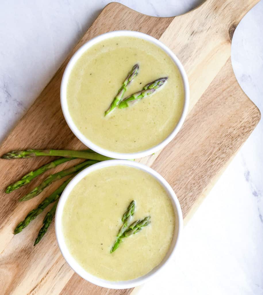 two bowls of asparagus soup on cutting board